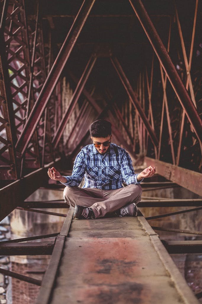 Young man meditates on a steel structure, embodying tranquility amidst urban architecture.